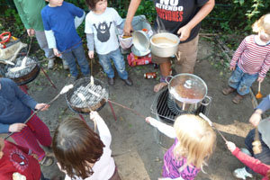 Kinder stehen um zwei Grill und einer Feuertonne herum